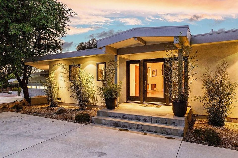 Mid-century modern home entry at dusk with cantilevered flat roof, warm uplighting and bamboo planters, remodeled in Ojai, California