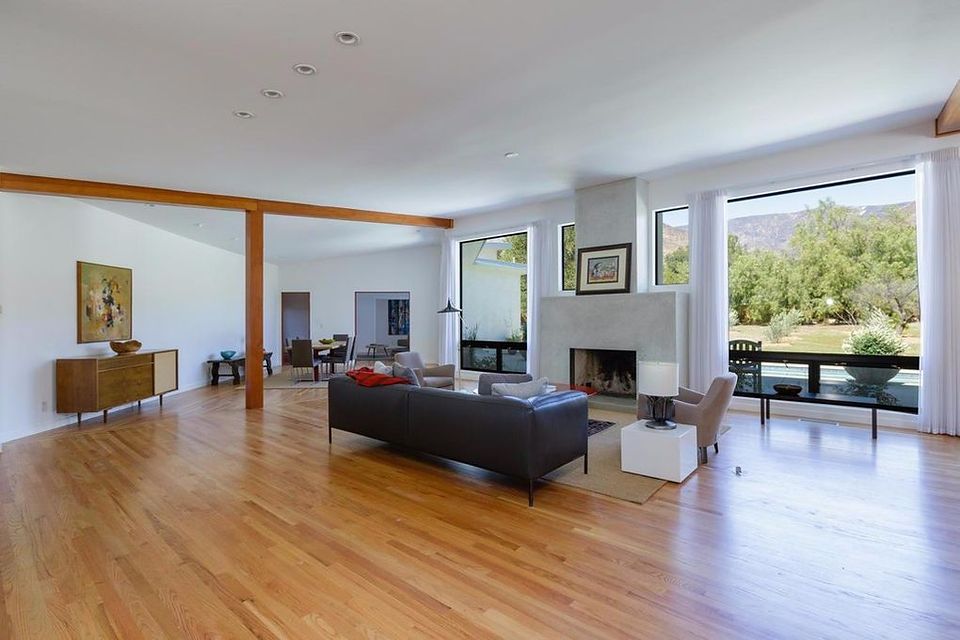 Open-plan living room with red oak floors, exposed timber beams, plaster fireplace and floor-to-ceiling windows onto the mountains