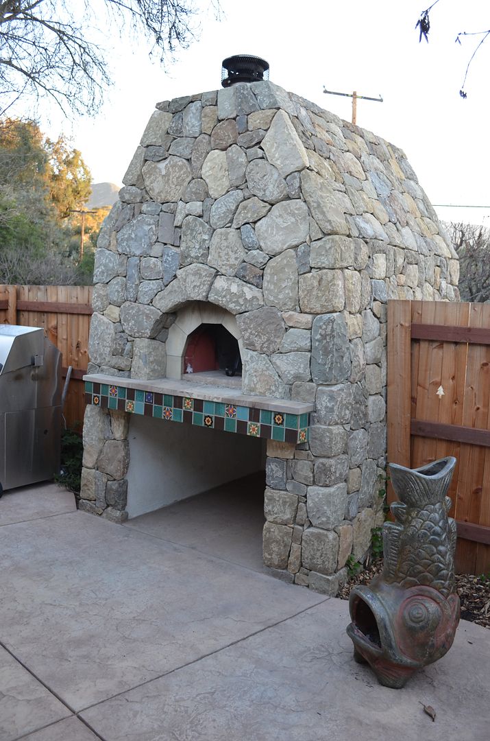 Hand-laid stone wood-fired pizza oven with tiled counter on a stamped concrete patio